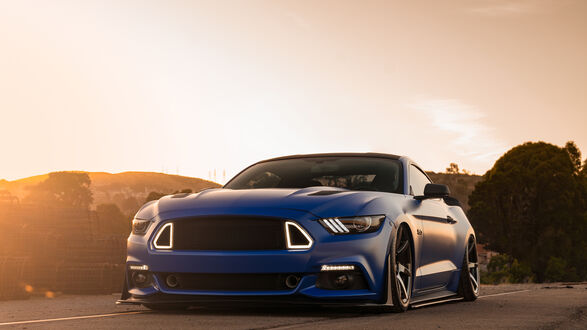 Обои на рабочий стол Ford mustang gt синего цвета стоит на дороге в лучах заката