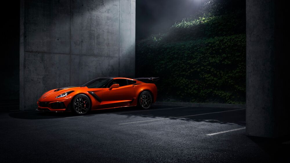 Обои для рабочего стола Оранжевый Chevrolet Corvette у бетонной стены на парковке