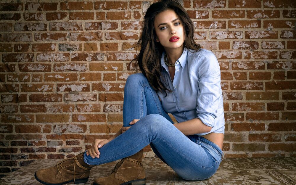 Обои для рабочего стола Irina Shayk в джинсах, в джинсовой рубашке и джинсах сидит на фоне кирпичной стены