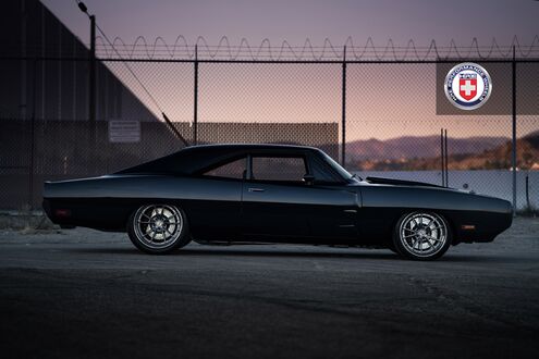 Обои на рабочий стол Черный Dodge Charger стоит на стоянке на фоне ограды рабицы