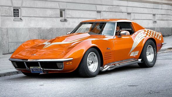 Обои на рабочий стол Оранжевый Chevrolet Corvette Stingray на фоне каменного здания на удице