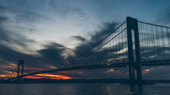 Обои на рабочий стол Мост Верразано-Нарроуз / Verrazano-narrows Bridge с массивными опорами и подвесными тросами на фоне закатного неба с темными облаками в Нью-Йорк / New York