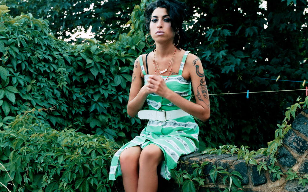 Обои для рабочего стола Amy Winehouse в зеленом сарафане сидит в окружении растений