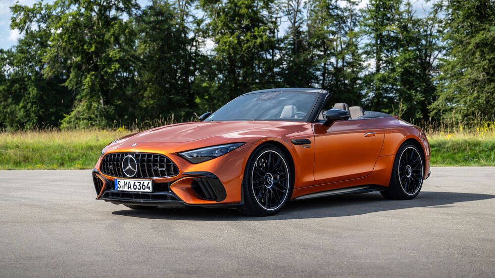 Обои для рабочего стола Оранжевый автомобиль Mercedes-AMG SL 63 S E Performance 2024 года на асфальте на фоне деревьев спереди