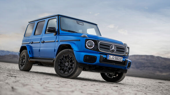 Обои на рабочий стол Синий внедорожник Mercedes-Benz G 580 With EQ Technology Edition One 2024 года с черными колесными дисками стоит на песчаной равнине на фоне гор и облачного неба