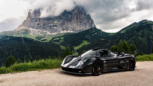 Обои на рабочий стол Спортивный автомобиль Pagani Zonda Cinque Roadster черного цвета стоит на дороге на фоне горного пейзажа в солнечный день в Альпах / Alps, Италия / Italy