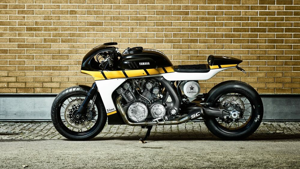 Обои для рабочего стола Черно-желтый мотоцикл V max Yamaha с округлыми обводами стоит у кирпичной стены на асфальте