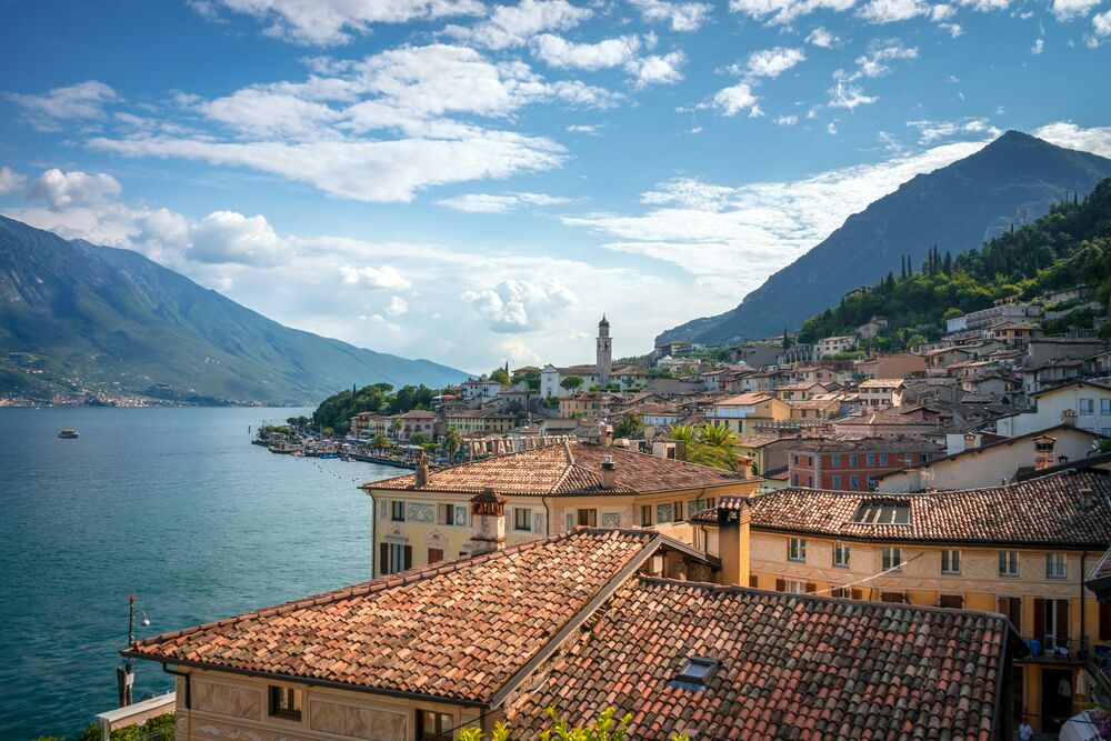 Обои для рабочего стола Город Лимоне-суль-Гарда / Limone sul Garda находится у озера Гарда на фоне гор Италия / Italy в солнечный день