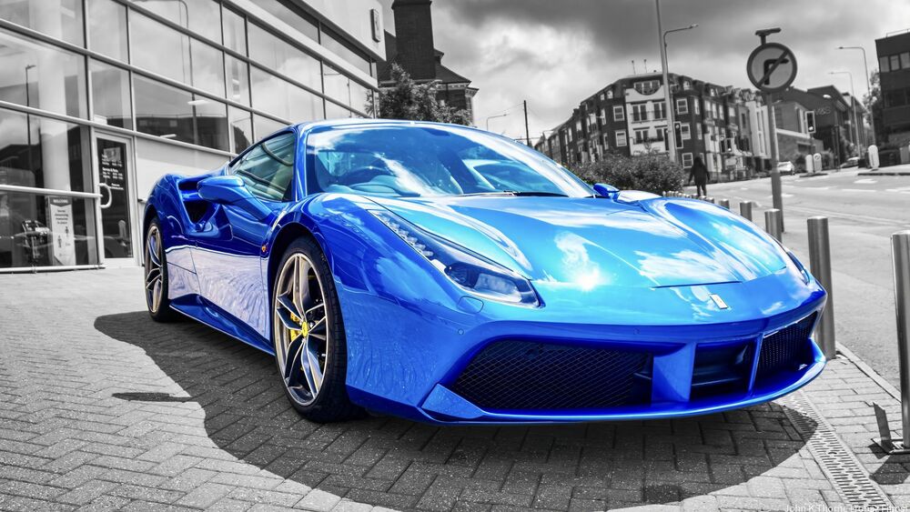 Обои для рабочего стола Синий автомобиль Ferrari 488 стоит на улице города в солнечную погоду на фоне зданий