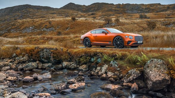 Обои на рабочий стол Bentley оранжевого цвета стоит на дороге на фоне холмов в пасмурную погоду