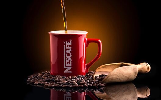 Обои на рабочий стол Красная кружка Nescafe с кофе рядом с деревянной лопаткой и кофейными зернами