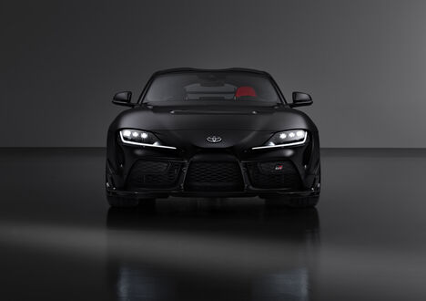 Обои на рабочий стол Toyota Supra A90 / Тойота Супра А90 Final Edition черного цвета стоит в затемненном помещении на сером фоне вид спереди