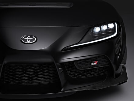 Обои на рабочий стол Фара и часть капота Toyota GR Supra A90 Final Edition 2025 черного цвета на темном фоне