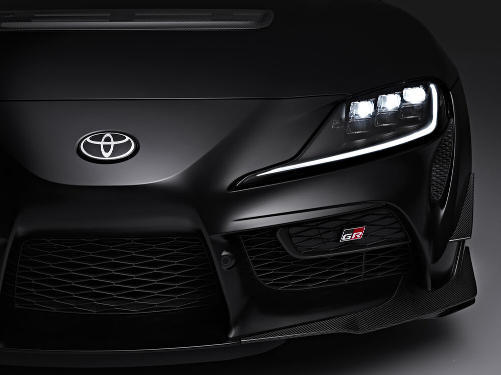Обои для рабочего стола Фара и часть капота Toyota GR Supra A90 Final Edition 2025 черного цвета на темном фоне