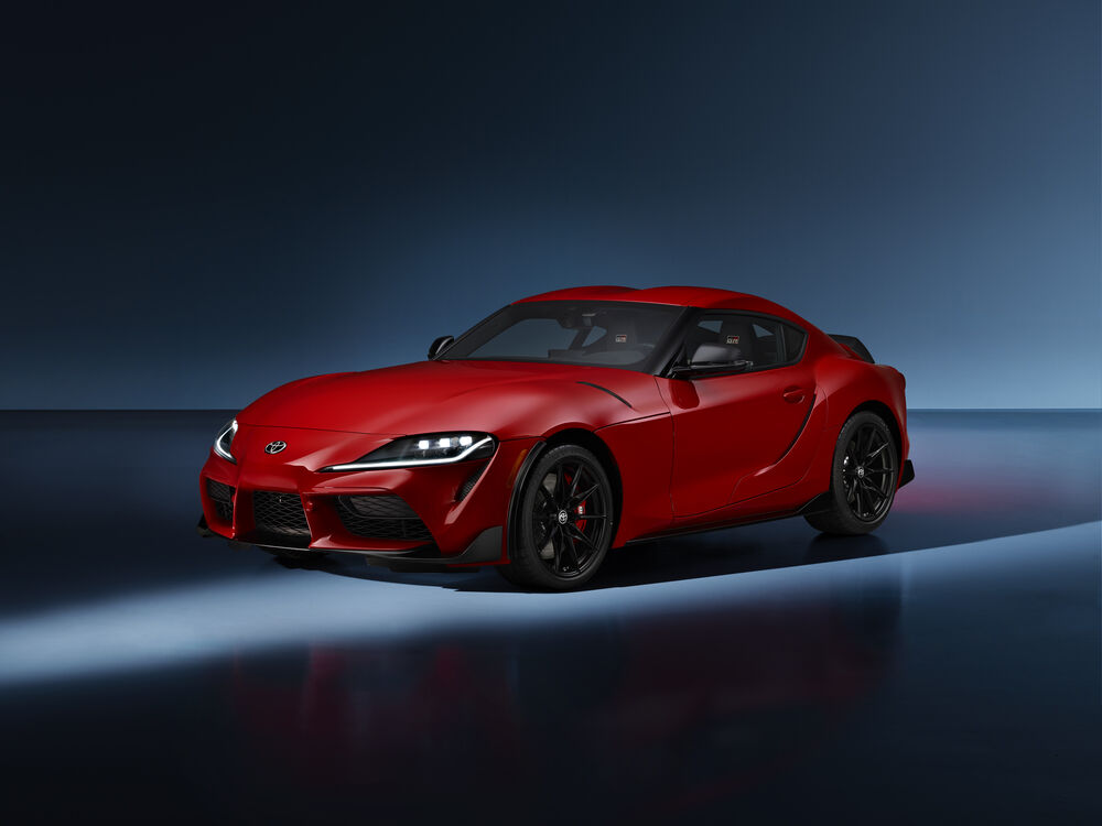 Обои для рабочего стола Toyota GR Supra Lightweight EVO 2025 красного цвета стоит на сером фоне под лучами прожектора