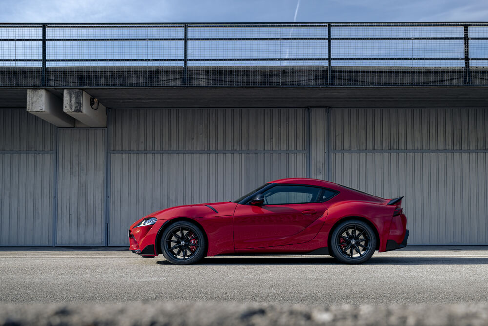 Обои для рабочего стола Toyota GR Supra Lightweight EVO 2025 в красном окрасе сбоку у серого здания