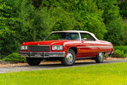Обои на рабочий стол Красный кабриолет Chevrolet / Шевроле Caprice / Каприс Classic / Классик стоит на зеленой лужайке на фоне деревьев днем
