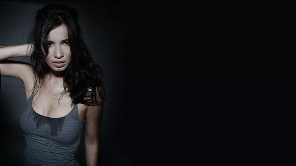 Обои на рабочий стол Селина Джейд / Celina Jade с длинными темными волосами в сером топе стоит на темном фоне