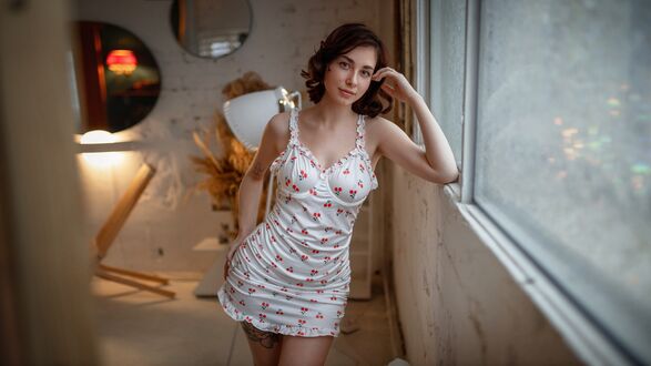 Обои на рабочий стол Модель Маргарита в светлом платье с вишенками стоит в комнате, облокотившись на окно