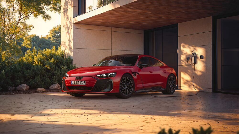 Обои для рабочего стола Автомобиль Audi / Ауди E-tron GT красного цвета заряжается у дома на фоне зелени в вечернее время