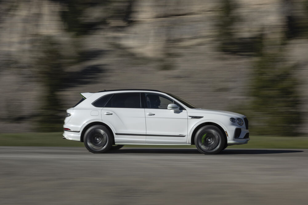 Обои для рабочего стола Автомобиль Bentley Бентайга белого цвета движется по дороге на фоне скалистого склона