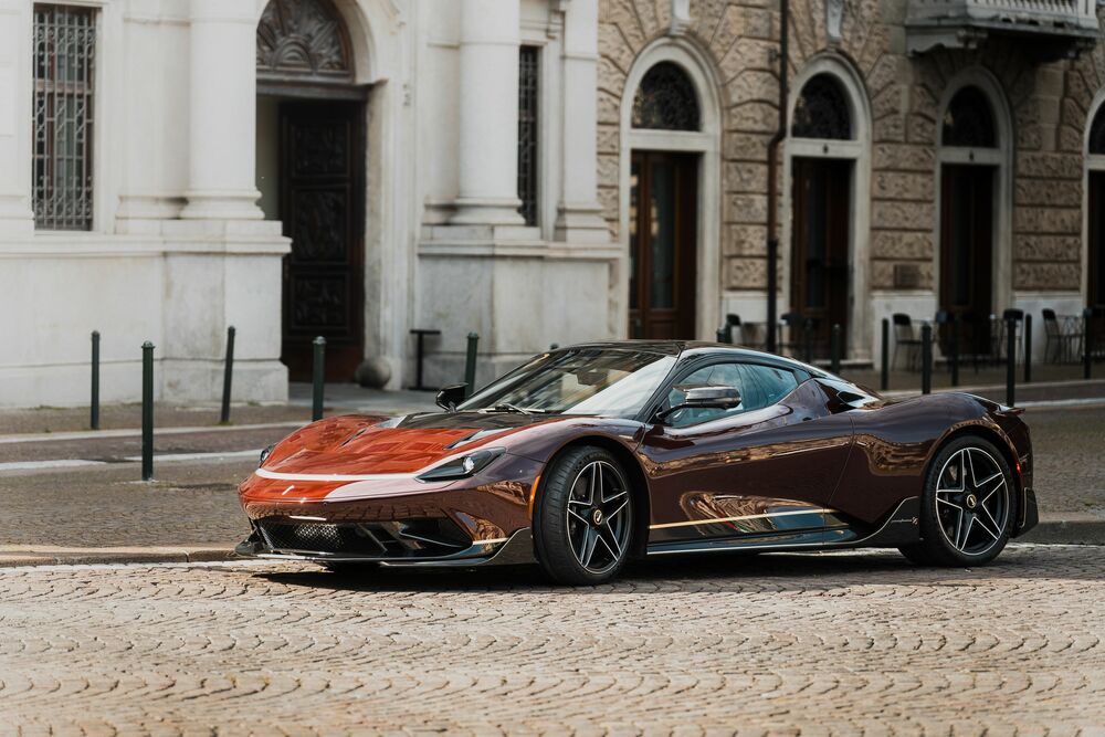 Обои для рабочего стола Автомобиль Automobili Pininfarina Battista темно-коричневого цвета на каменной мостовой на фоне здания