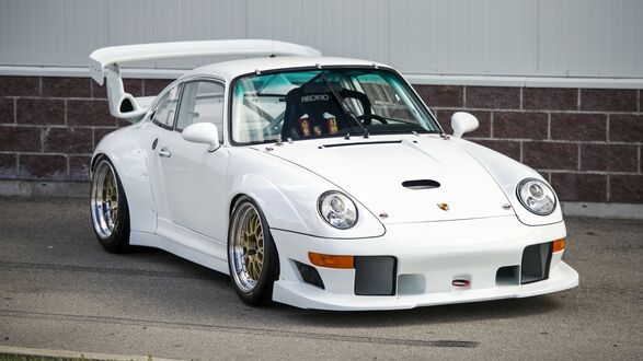 Обои на рабочий стол Спортивный автомобиль Porsche GT2 Evo белого цвета стоит на парковке на фоне кирпичной стены
