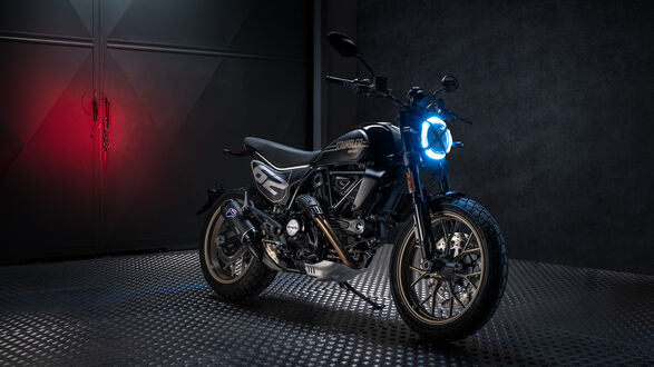 Обои на рабочий стол Мотоцикл Ducati Scrambler черного цвета с ярко-синей круглой фарой стоит на металлической поверхности на темном фоне с красным свечением