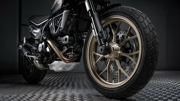 Обои на рабочий стол Переднее колесо мотоцикла Ducati Scrambler с золотистым диском и черной шиной крупным планом стоит на рифленом полу в студии на темном фоне