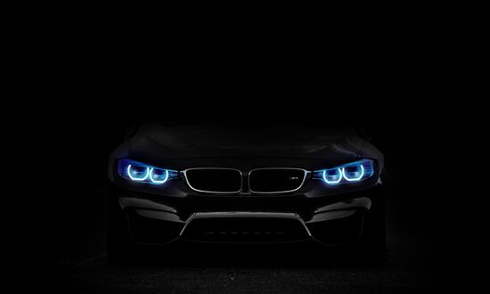 Обои на рабочий стол Черный автомобиль BMW с ярко-синими светодиодными фарами стоит, демонстрируя свою переднюю часть на черном фоне