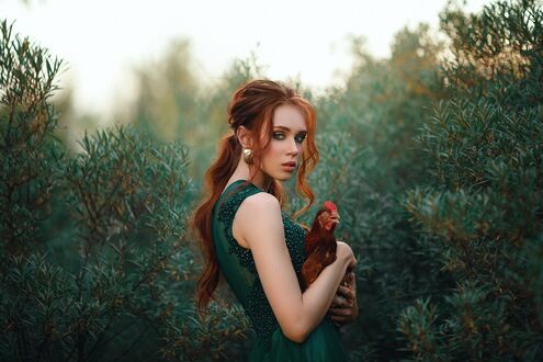 Обои на рабочий стол Модель Anna Churakova в зеленом платье и с курочкой в руках стоит среди кустов на природе