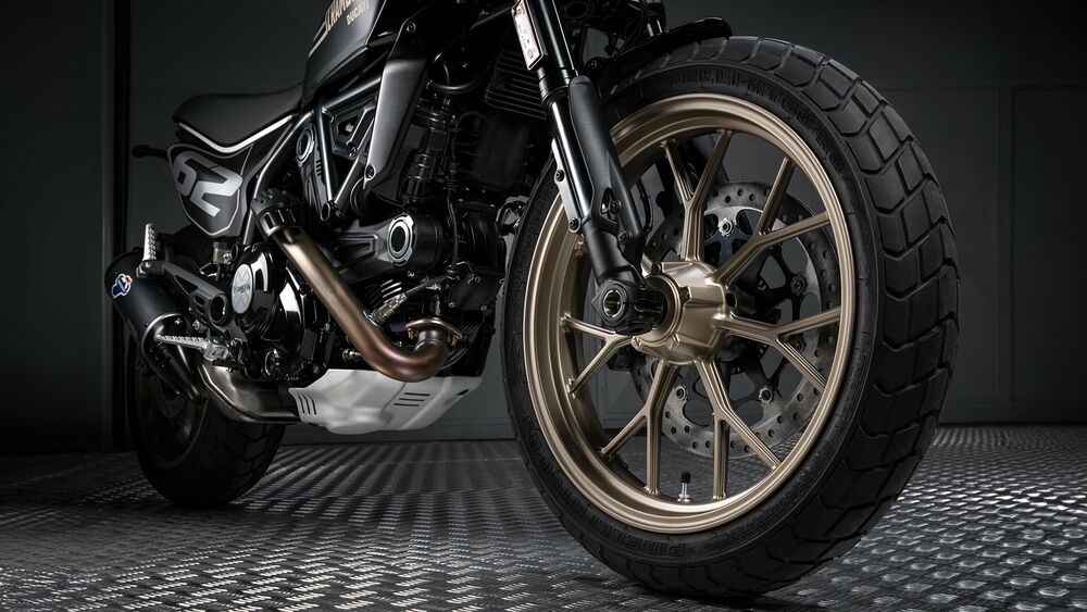 Обои для рабочего стола Переднее колесо мотоцикла Ducati Scrambler с золотистым диском и черной шиной крупным планом стоит на рифленом полу в студии на темном фоне