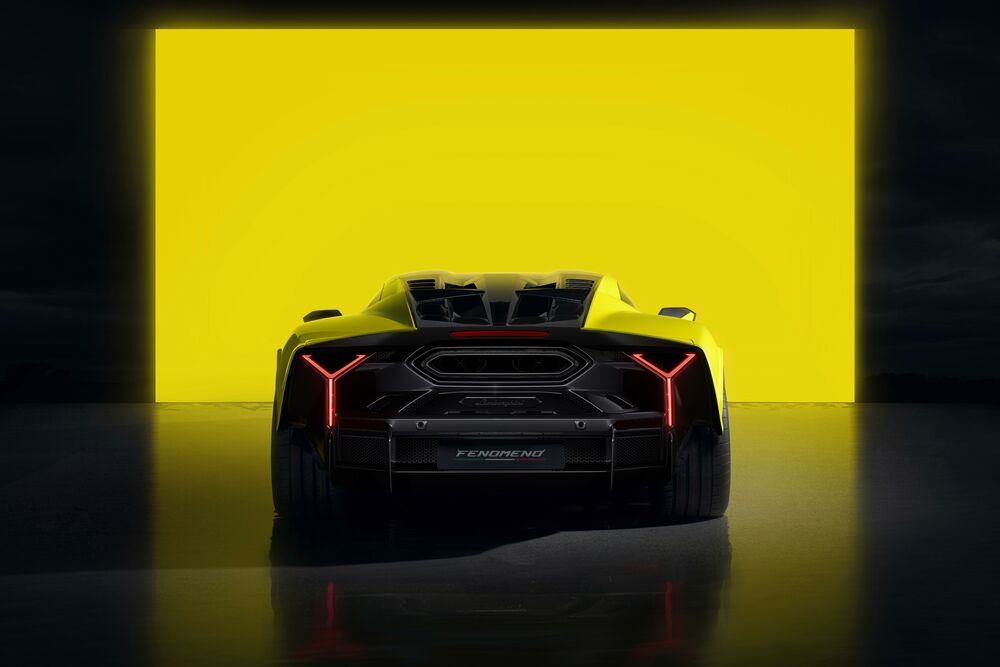 Обои для рабочего стола Желтый и черный Lamborghini Fenomeno с красными Y-образными задними фонарями вид сзади, стоит на темном полу, на фоне большого светящегося желтого прямоугольника