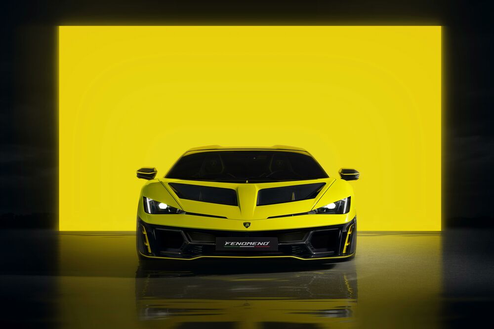 Обои для рабочего стола Желтый Lamborghini Fenomeno с включенными фарами на отражающемся полу на фоне яркой желтой стены вид спереди