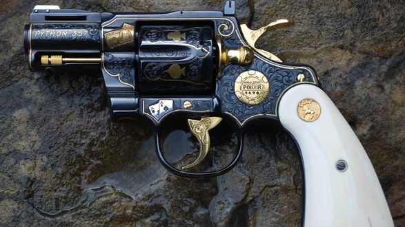 Обои на рабочий стол Черный револьвер Colt Python с золотыми гравировками и белой рукоятью лежит на мокрой темной текстурированной поверхности, на нем надписи (PYTHON 357) и (WORLD SERIES OF POKER)