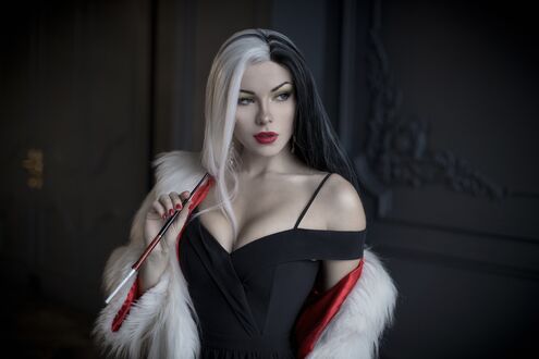 Обои на рабочий стол Девушка в образе Круэллы / Cruella из фильма Круэлла / Cruella позирует в черном платье и белой меховой накидке, держа мундштук, на фоне темной стены с декоративным элементом