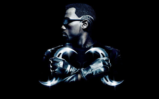 Обои на рабочий стол Уэсли Снайпс / Wesley Snipes из фильма Блэйд / Blade в темных очках и кожаном костюме скрестил руки, держащие два изогнутых клинка, на черном фоне