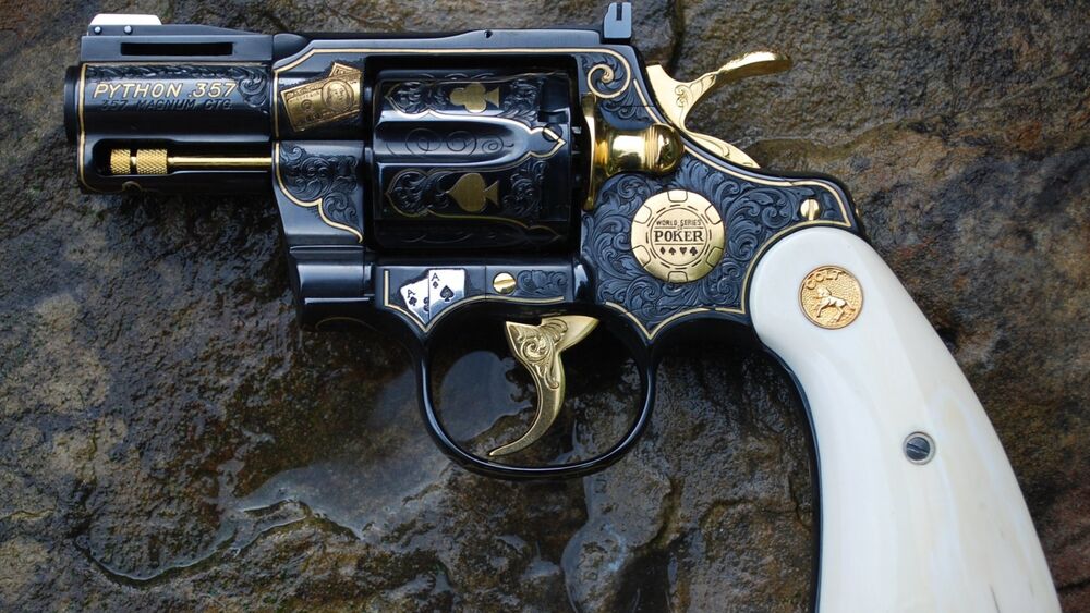 Обои для рабочего стола Черный револьвер Colt Python с золотыми гравировками и белой рукоятью лежит на мокрой темной текстурированной поверхности, на нем надписи (PYTHON 357) и (WORLD SERIES OF POKER)