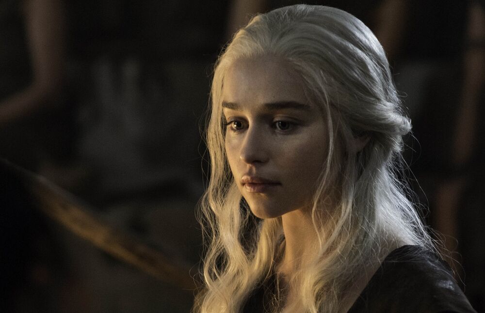Обои для рабочего стола Портрет Эмилии Кларк / Emilia Clarke из фильма Игра престолов / Game of Thrones, с длинными светлыми волосами, смотрящей вниз и в сторону, на размытом темном фоне