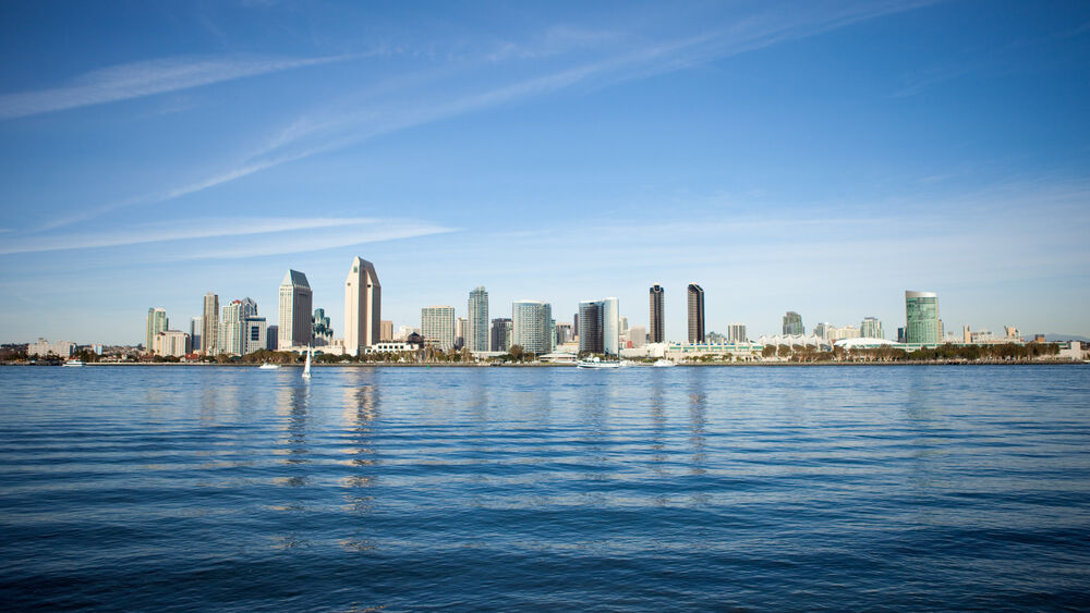 Обои для рабочего стола Сан-Диего / San Diego, Калифорния / California, США / USA, синяя вода с рябью на переднем плане, на фоне городской пейзаж с высотными зданиями и несколькими лодками под ясным небом