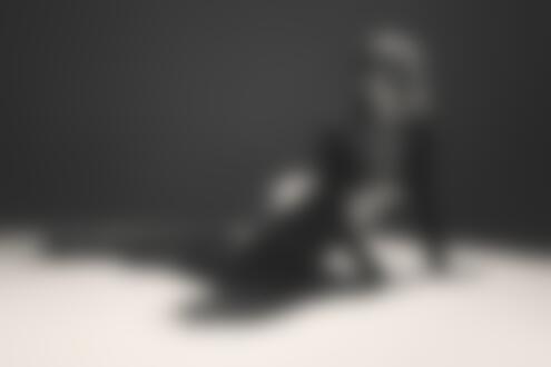 Обои на рабочий стол Девушка в черном костюме и высоких сапогах позирует на полу, на фоне темной студии с направленным светом
