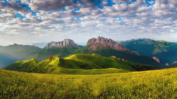 Обои на рабочий стол Адыгея / Adygea, Россия / Russia, зеленый травянистый склон на переднем плане, на фоне гор Западный Ачешбок / Western Acheshbok и Восточный Ачешбок / Eastern Acheshbok под голубым небом с облаками