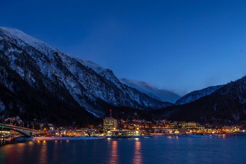 Обои на рабочий стол Джуно / Juneau, США / USA, огни города отражаются в темной воде залива, мост пересекает канал, на фоне заснеженных гор и темного неба