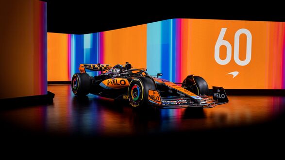 Обои на рабочий стол McLaren F1 гоночный автомобиль черного и оранжевого цвета на темном полу, (VELO, chrome) на фоне светящихся панелей с оранжевыми и синими полосами и числом (60)
