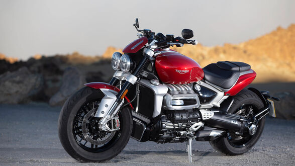Обои на рабочий стол Красный с серебристыми элементами мотоцикл Triumph Rocket III припаркован на дороге, на фоне каменистых холмов