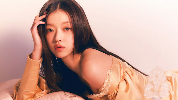 Обои на рабочий стол Портрет YooA из Oh My Girl позирует, лежа на светлой подушке в золотистом платье, на фоне светлой стены