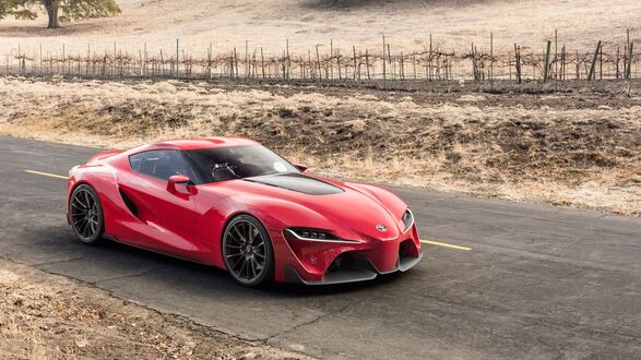 Обои на рабочий стол Красный спортивный автомобиль Toyota Supra едет по асфальтированной дороге с желтой разметкой, на фоне сухих холмов с виноградником и редкими деревьями