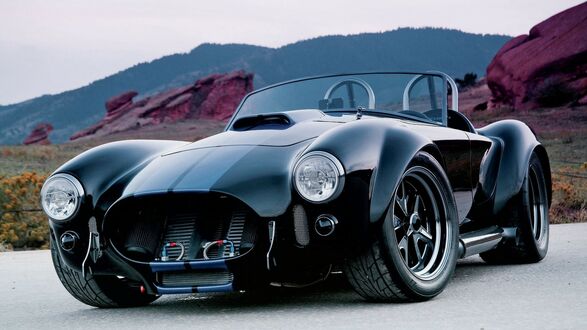 Обои на рабочий стол Черный автомобиль Ac Cobra / Shelbi с синими полосами припаркован на дороге, на фоне гор с красными скалами и редкой растительностью под пасмурным небом