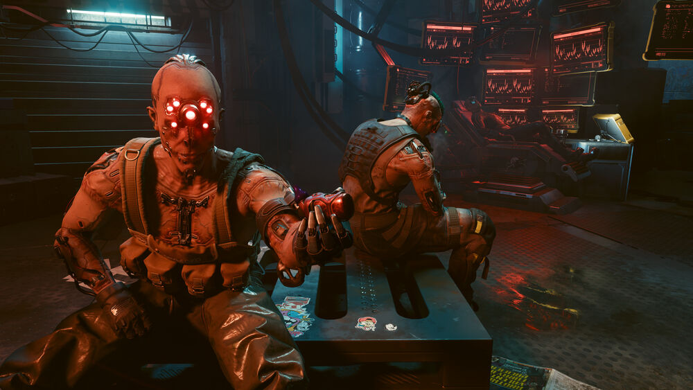 Обои для рабочего стола Дум-Дум / Dum-Dum из Мальстрем / Maelstrom из игры Cyberpunk 2077 / Cyberpunk 2077 с красными кибернетическими глазами держит красный предмет, рядом другой персонаж на фоне темного помещения с экранами и проводами