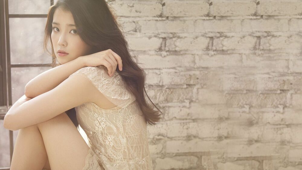 Обои для рабочего стола Певица Lee Ji-eun, IU, / Ли Джиын, АйЮ в светлом кружевном платье позирует, обхватив колени руками, на фоне кирпичной стены и оконной рамы